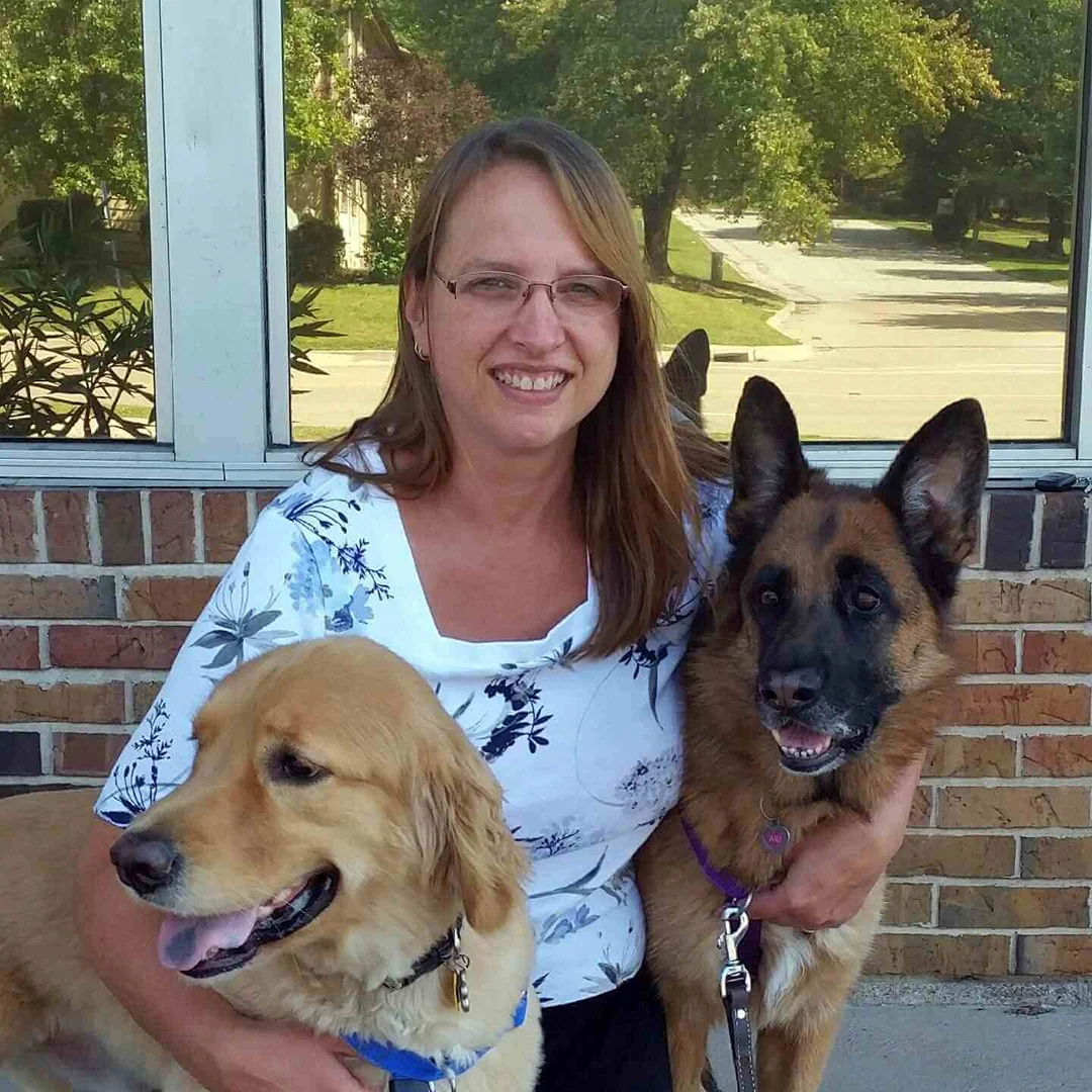 Dr. Karin Crocker Dr. Karin Crocker sitting outside with a golden retriever and a German shepherd